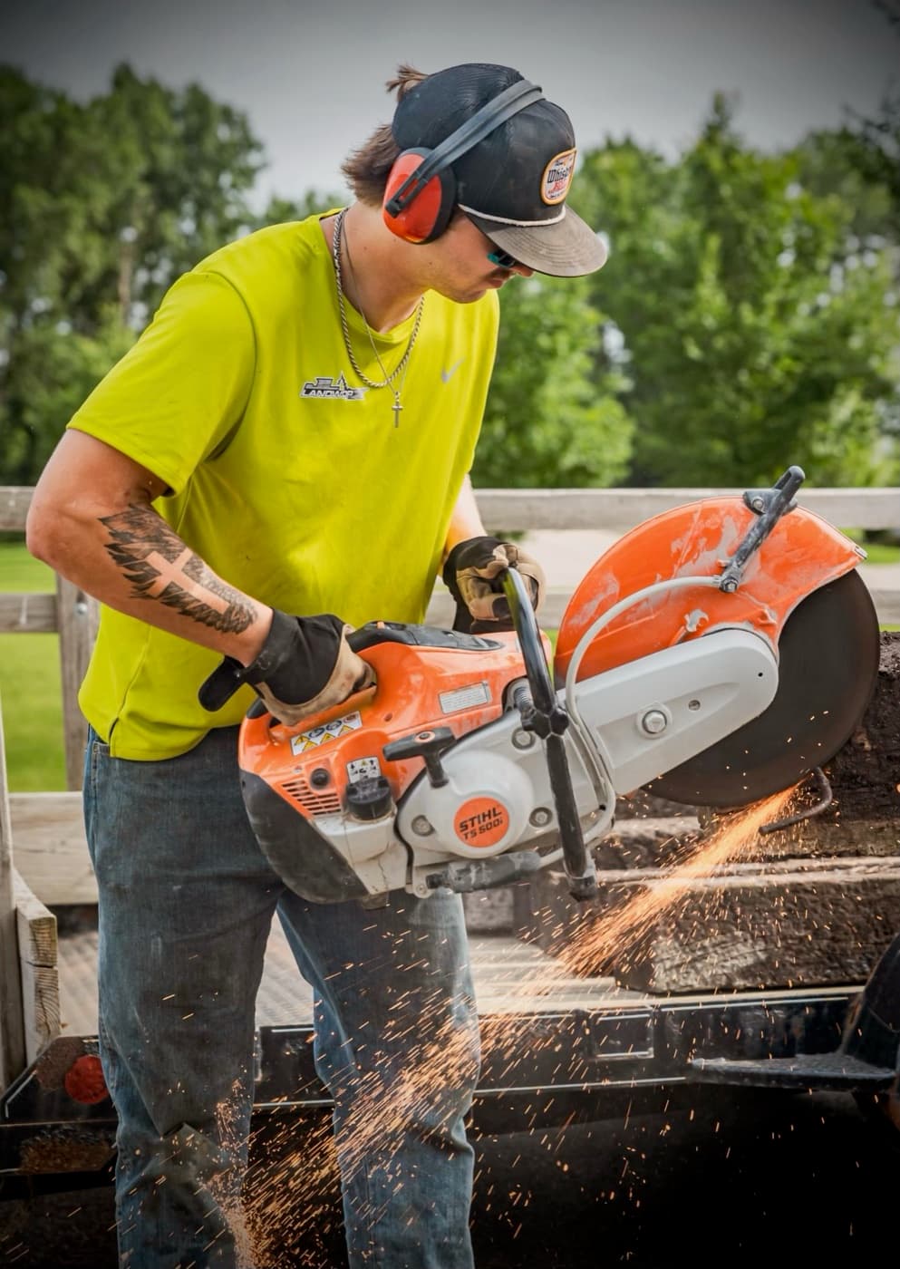 Crew member in a JL Landworx shirt cutting steel with a cut-off saw